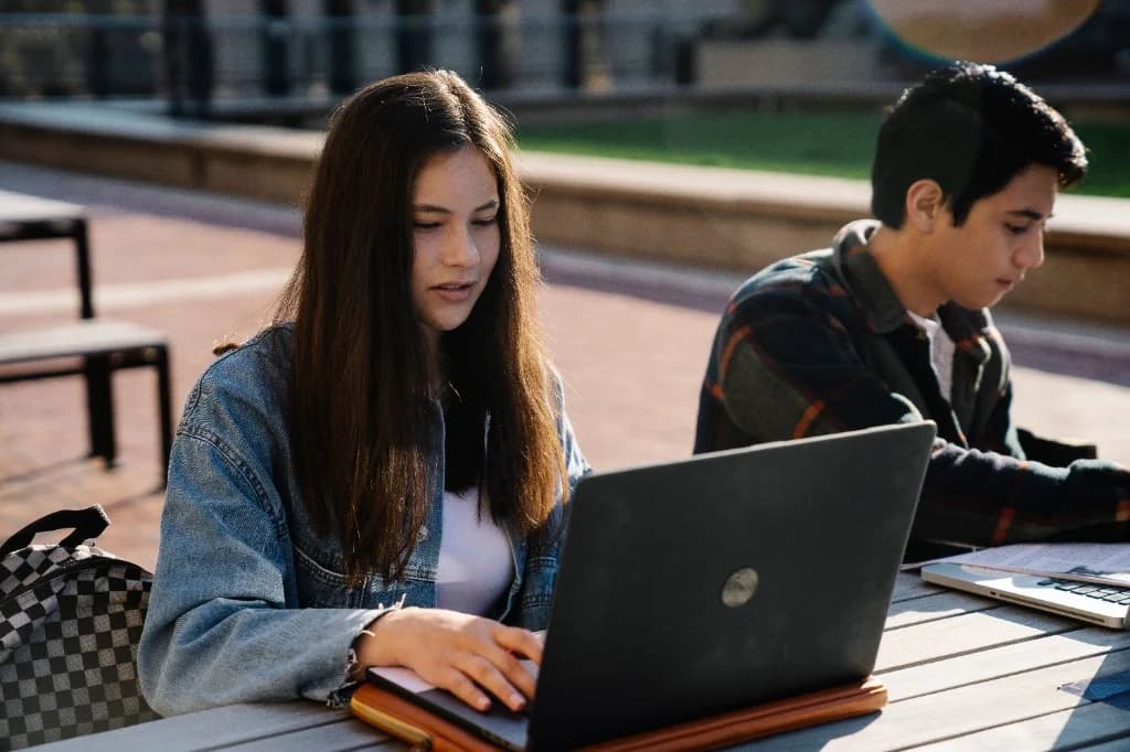 Two students taking digital ACT practice tests on laptops outdoors