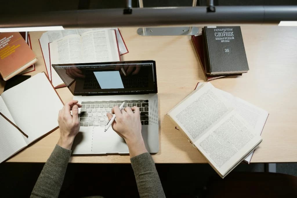 Student working at a desk with a laptop and reference books